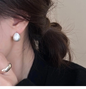 Close-up of silver teardrop stud earrings with brushed texture on model's ear