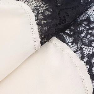 Détail de la dentelle noire sur tissu satin crème pour robe asymétrique