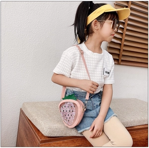 Pink strawberry crossbody bag for girls with glitter sequins worn by a child on a bench