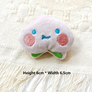 Detail view of pink peach plush brooch featuring embroidered face, size 6cm by 6.5cm