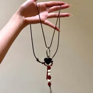 Detail of bohemian necklace featuring black heart charm and red key pendant on wax rope