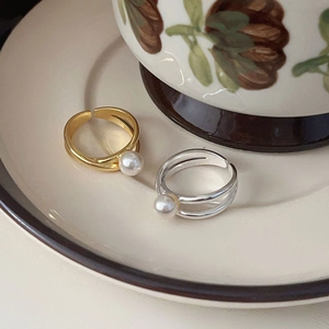 Crossed open 925 silver rings with pearls in gold and silver finish on ceramic tray