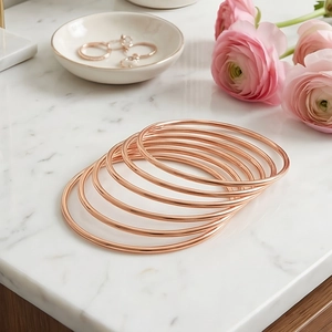 Stack of rose gold stainless steel bangles on a luxury white marble surface background