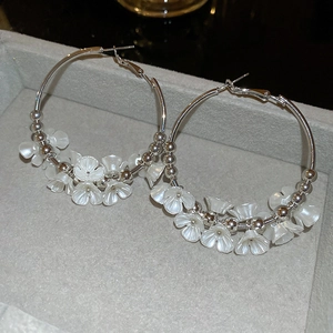 Detail view of large silver hoop earrings featuring white acrylic flower charms and beads