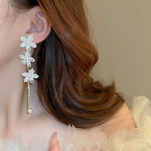 Close-up of white lily earrings with cascading pearl tassels and rhinestone detail