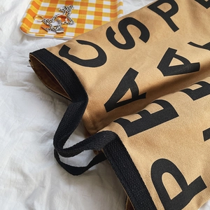 Detail of khaki canvas tote bag featuring large black lettering and durable webbed handles
