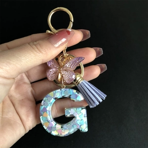Macro shot of resin letter G keychain with heart sequins, purple butterfly and tassel