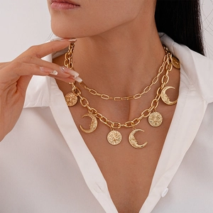 Detail of layered gold necklaces with sun and moon pendants worn on a white shirt