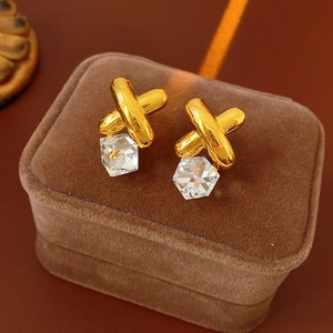 Close-up of vintage gold X-shaped earrings with clear hexagonal crystals on brown velvet