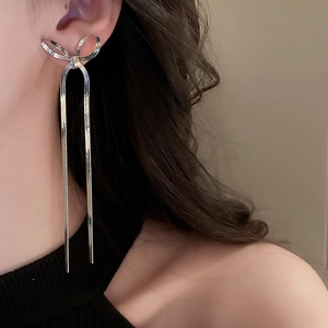 Side view detail of silver bow knot earrings with long snake chain tassels on a model