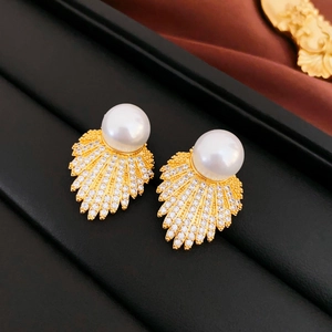 Close-up of fan-shaped pearl earrings with gold plating and zircon inlay on a black tray