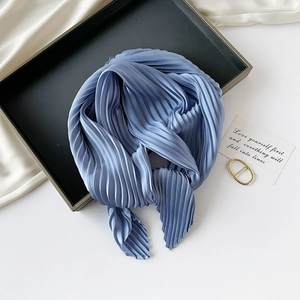 Artistic display of a blue pleated silk scarf on a tray with decorative props and card