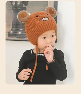 Détail du bonnet en tricot marron pour enfant avec oreilles à pompon et broderie