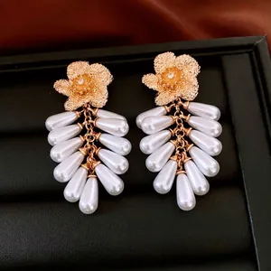 Golden flower earrings with zircon center and white pearl tassels on black leather stand