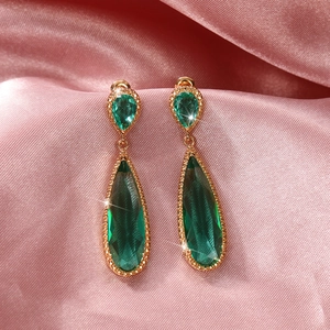 Detailed shot of gold drop earrings with faceted green gemstones on pink silk fabric