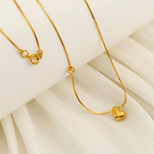 Detail of a gold-plated heart pendant necklace with a zircon accent on a silk background