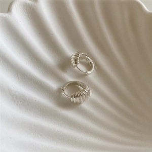 Detail of silver twisted croissant earrings inside a white shell-shaped ceramic plate