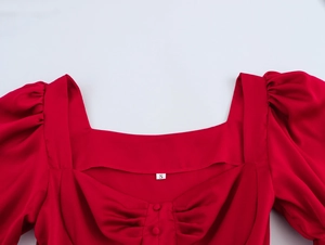 Detail van rode jurk met vierkante hals, pofmouwen en decoratieve stoffen knopen