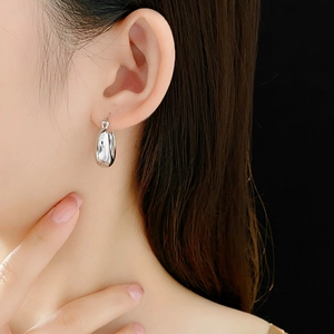Close-up of polished silver U-shaped hoop earring worn by a model on black background