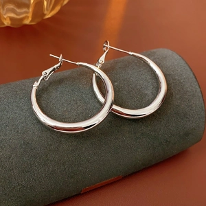 Macro shot of silver hoop earrings on a textured display stand with smooth metal finish