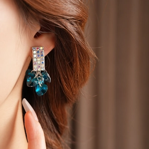 Detailed close-up of crystal tassel earrings with blue heart-shaped gems on a model