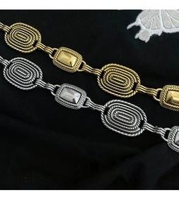 Détail de ceinture chaîne style ethnique montrant les textures métalliques tressées dorées