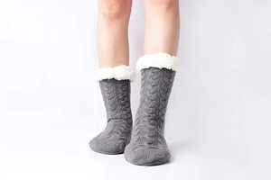 Detail of grey cable knit slipper socks with soft white faux fur trim on a model