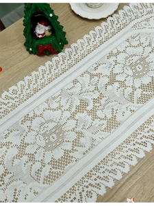 Close-up of white lace table runner with floral patterns and scalloped edges on wood