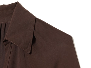 Macro detail of the dark brown pleated fabric texture and stitching on the midi dress collar