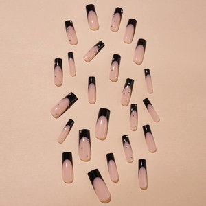 Long coffin fake nails featuring black French tips and crystal accents on beige background