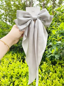 Macro detail of large grey satin bow hair clip with long ribbons on display card