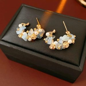 Macro view of C-shaped gold pearl earrings with blue stones and rose carvings
