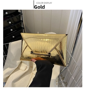 Detail of gold envelope clutch bag featuring glossy crocodile texture and metal bar clasp