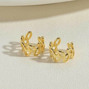 Close-up of golden hollow leaf ear cuffs with textured metal on minimalist background