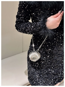 Detail of silver shell-shaped evening clutch with bead chain worn by a model