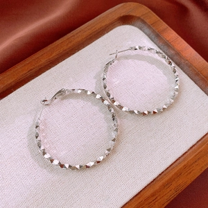 Detail of silver textured hoop earrings with faceted diamond-cut finish on silk
