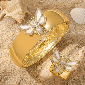 Golden bee jewelry set with white shell inlay and rhinestones on sandy beach background