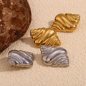 Close-up of conch shell earrings in gold and silver finish on a natural textured surface