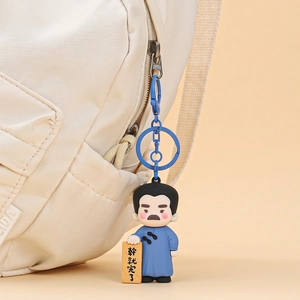 Schlüsselanhänger Cartoon-Figur mit blauem Gewand und Plakette an einer Stofftasche