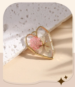 Detailed view of heart-shaped gold frame earring with pink resin-encapsulated dried flowers