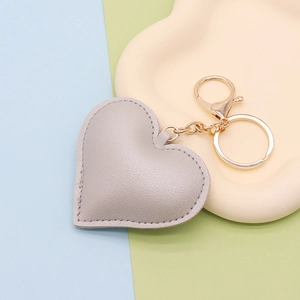 Macro detail of a grey heart-shaped PU leather keychain on a beige tray with gold hardware
