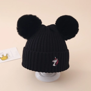 Detail of a black knit hat with double faux fur pom poms and unicorn embroidery for girls