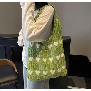 Detalle de bolso de hombro de punto verde con patrones de corazones blancos en modelo