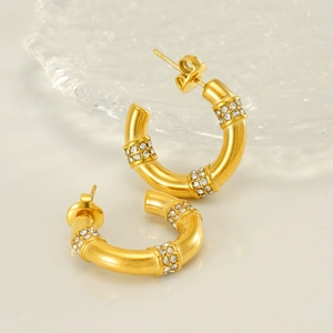 Gros plan de boucles d'oreilles créoles dorées ornées de bandes en zircon style bambou