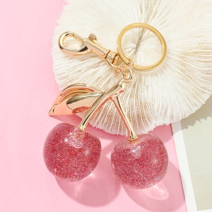 Close-up of glittery red cherry keychain with gold leaf detail and lobster clasp