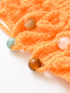 Detail of bright orange handmade knit fabric featuring colorful resin bead accents