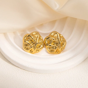 Close-up of golden geometric stud earrings with irregular wrinkled metal texture on silk