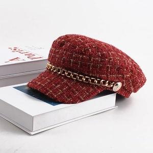 Close-up of red tweed baker boy hat featuring a thick gold chain and embossed metal button