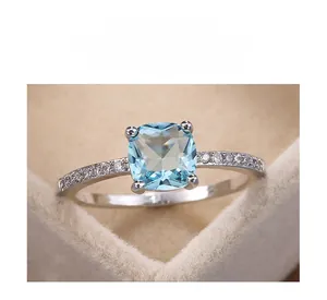 Macro view of blue cushion-cut zircon ring with side micro-pave diamonds in a velvet box