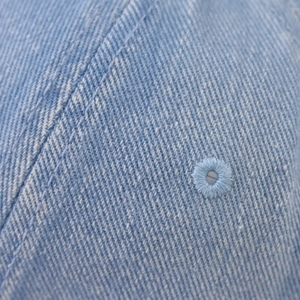 Close-up of light blue washed denim fabric with fine stitching and embroidered eyelet detail